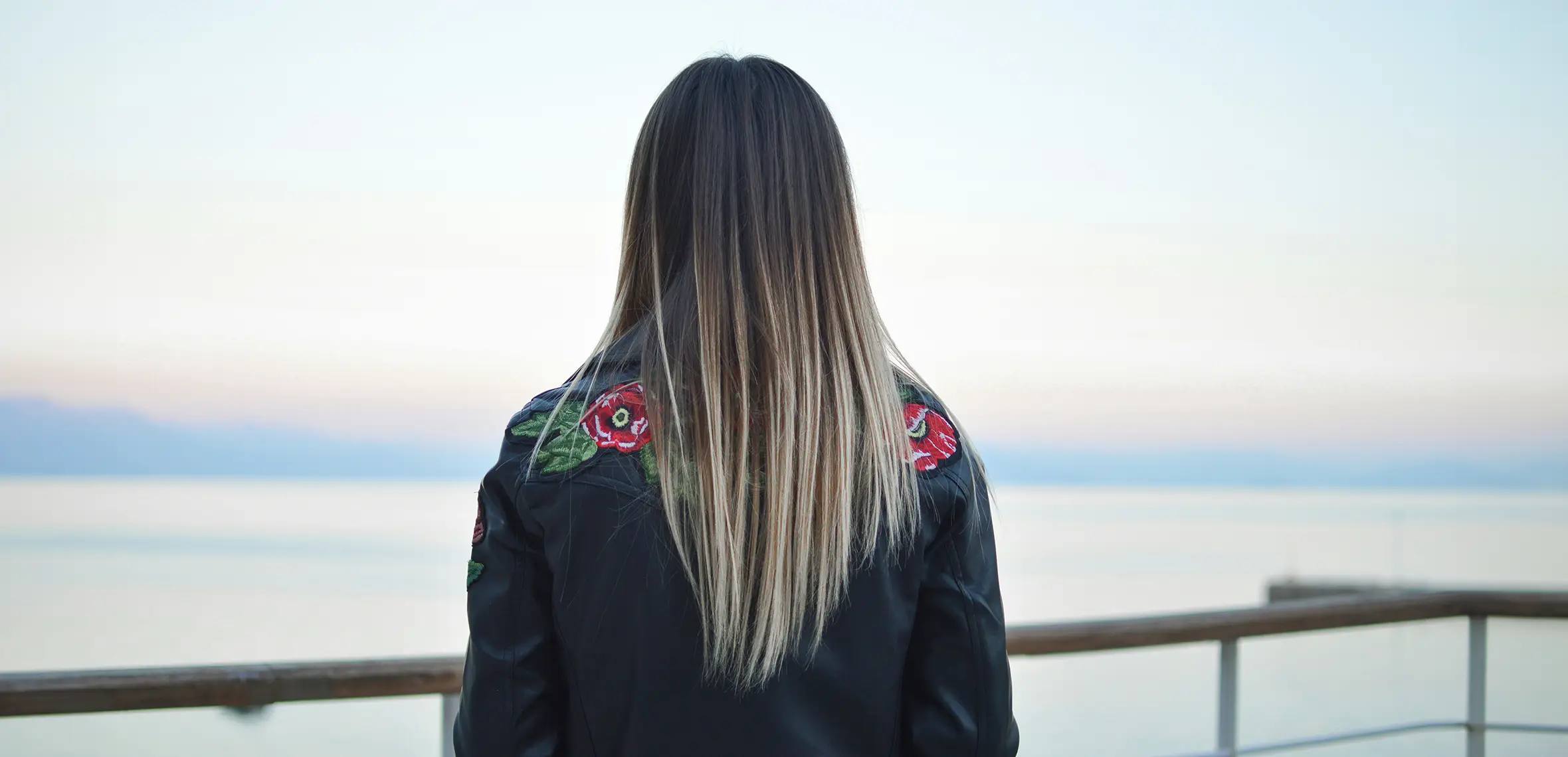 Back of head view of a woman with blonde hair looking out at the sea