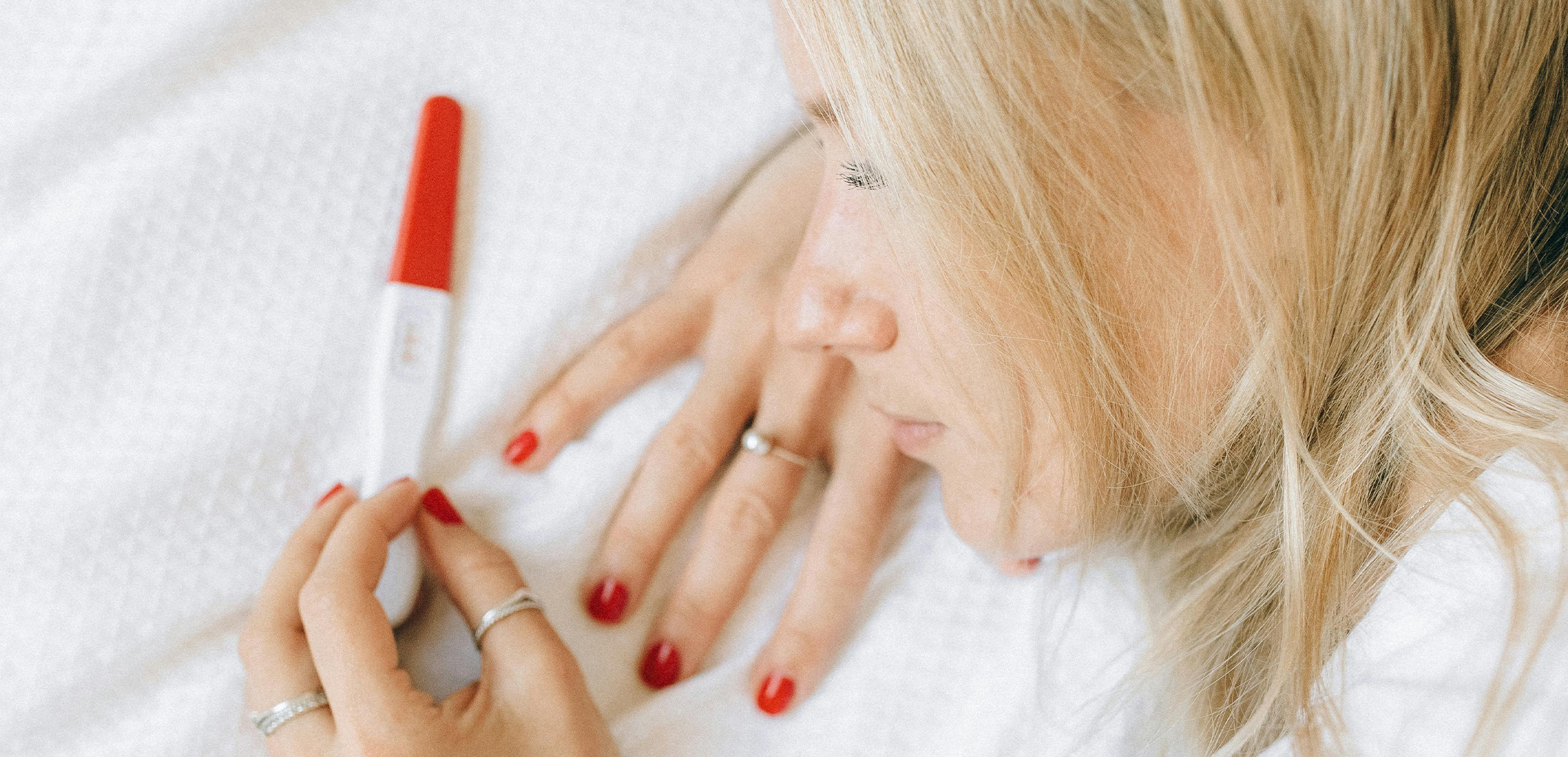 woman on bed looking at a pregnancy test